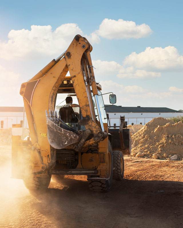 Backhoe loader working red earth on a South African site, operator in the cab