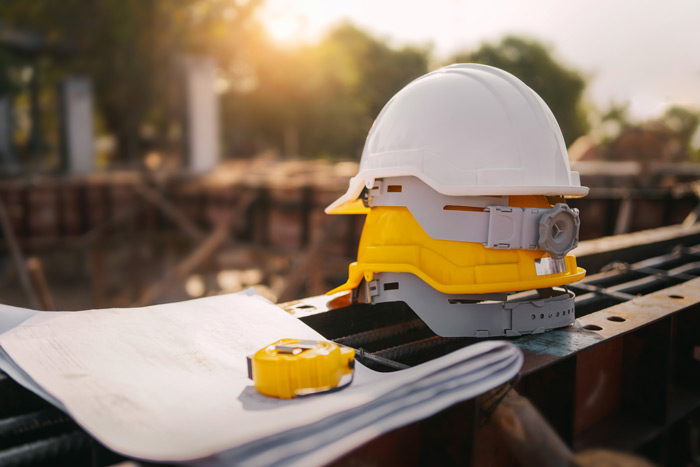 A stack of hard hats, site plans and a tape measure resting on steel formwork, with the site out of focus behind